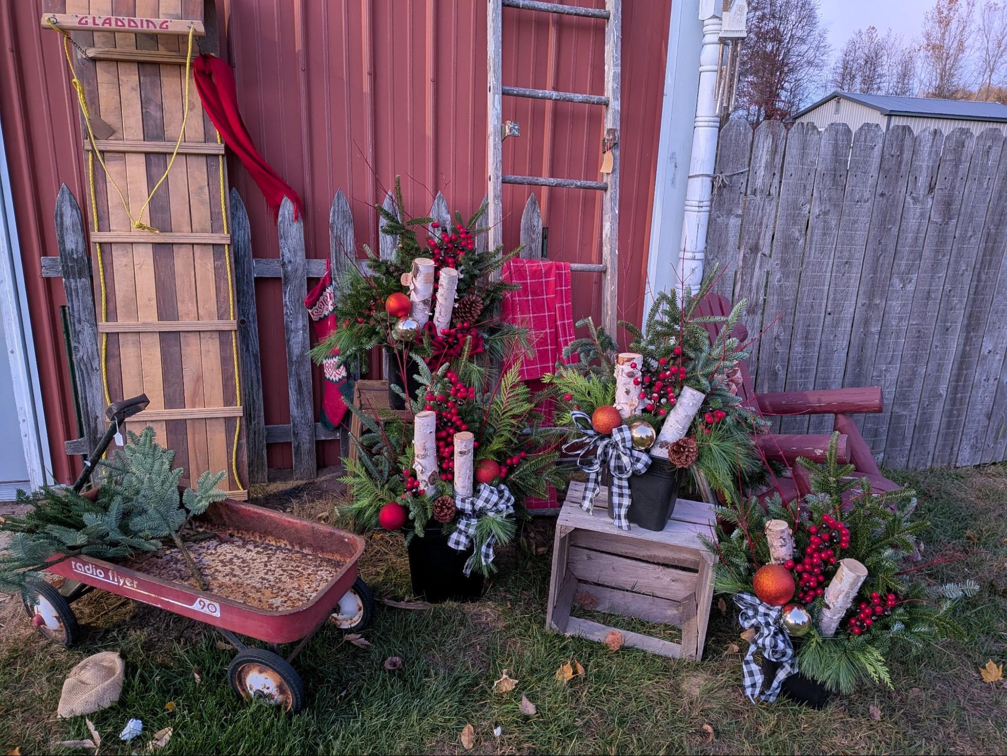 Christmas porch pots with birch logs, berries, and plaid bows beside a red barn